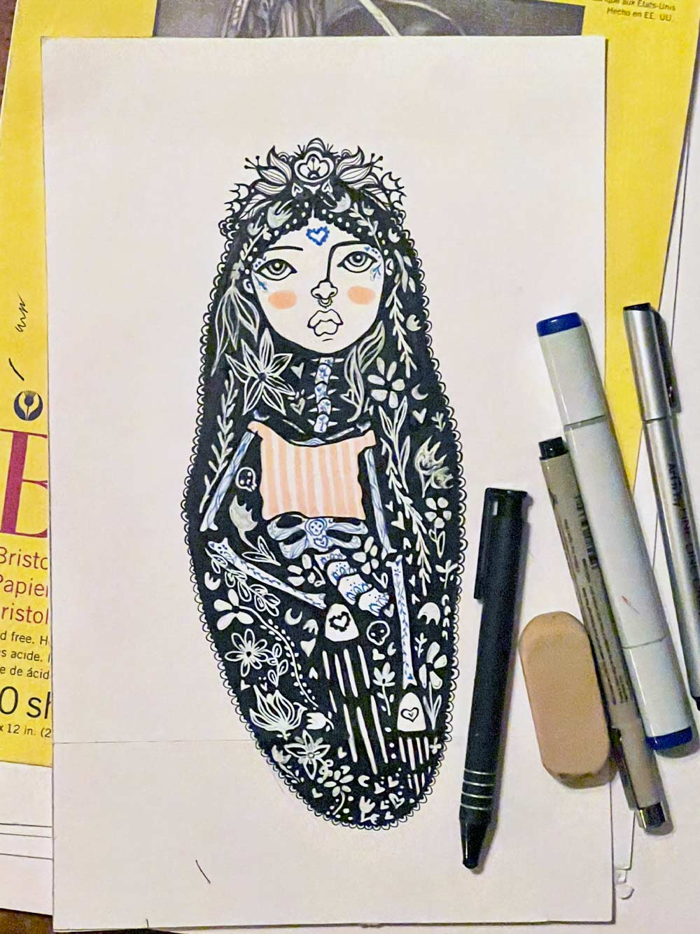 Illustration of a stylized face with floral patterns on a piece of paper with art supplies.
