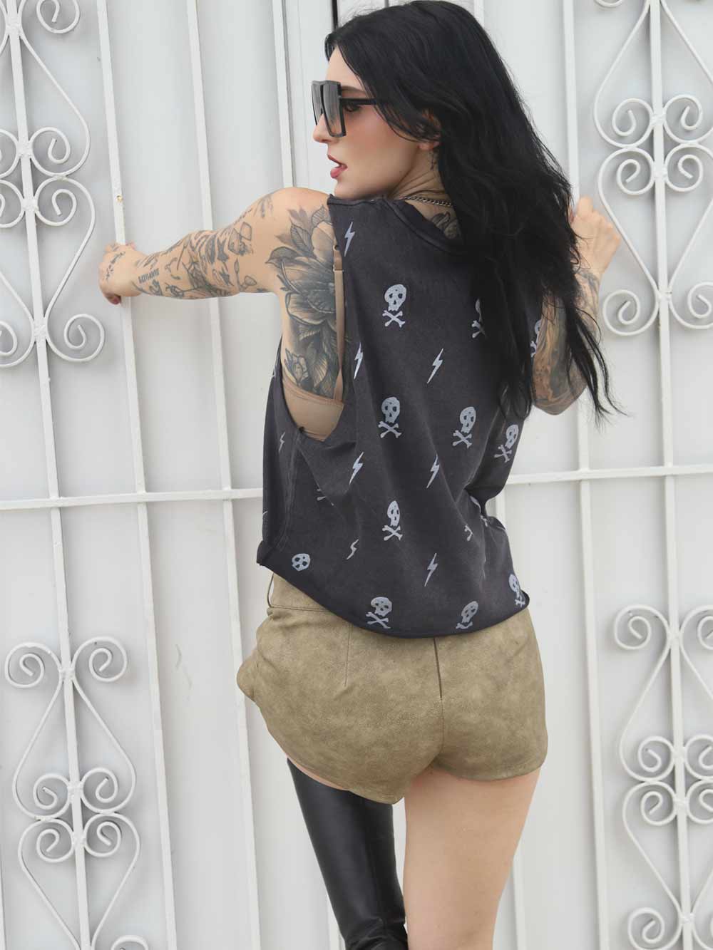 Woman wearing a black crop top with skull patterns grabbing a white decorative wall.
