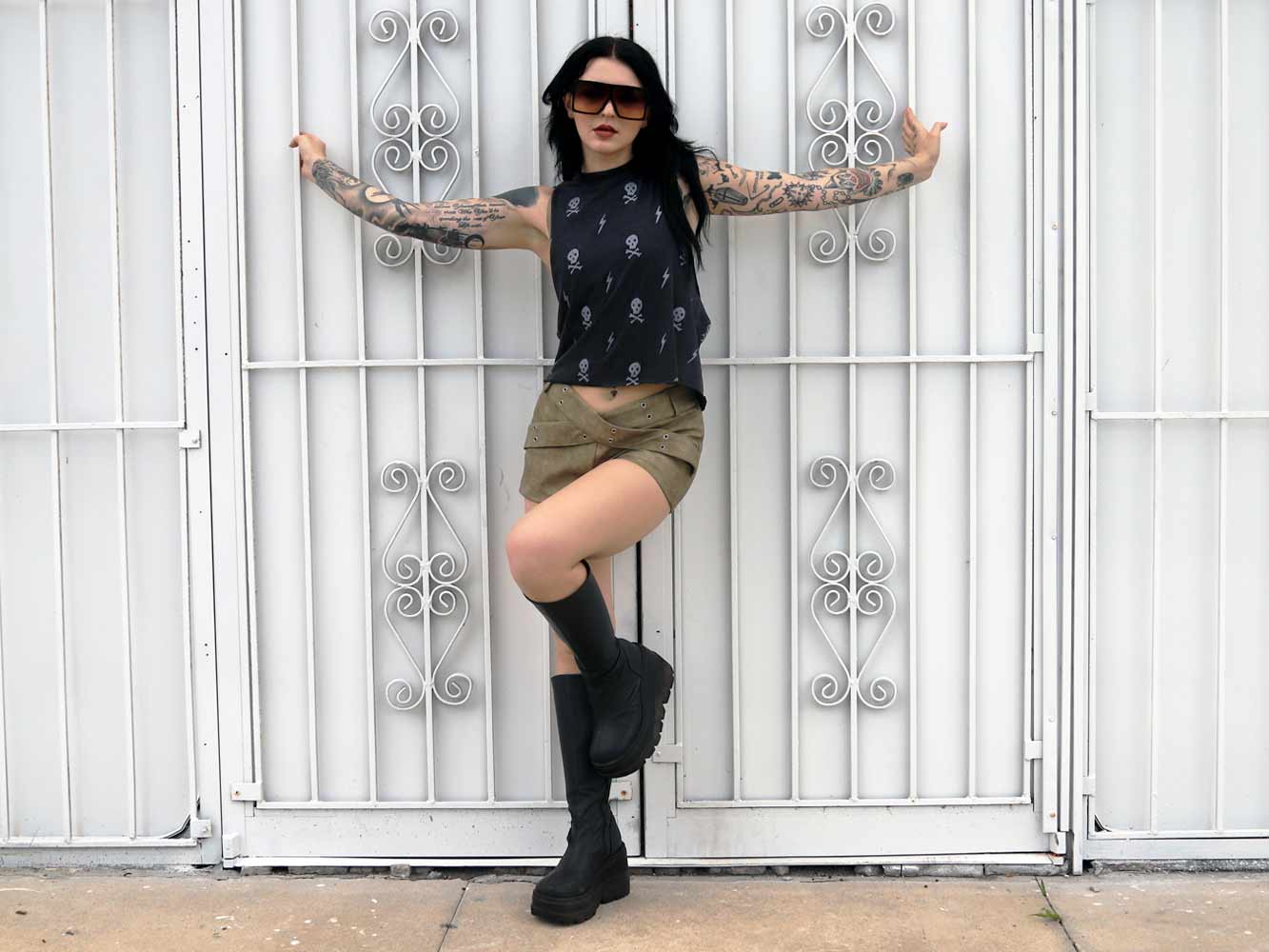 Girl with tattoos wearing a black crop top with skull & Crossbones design.