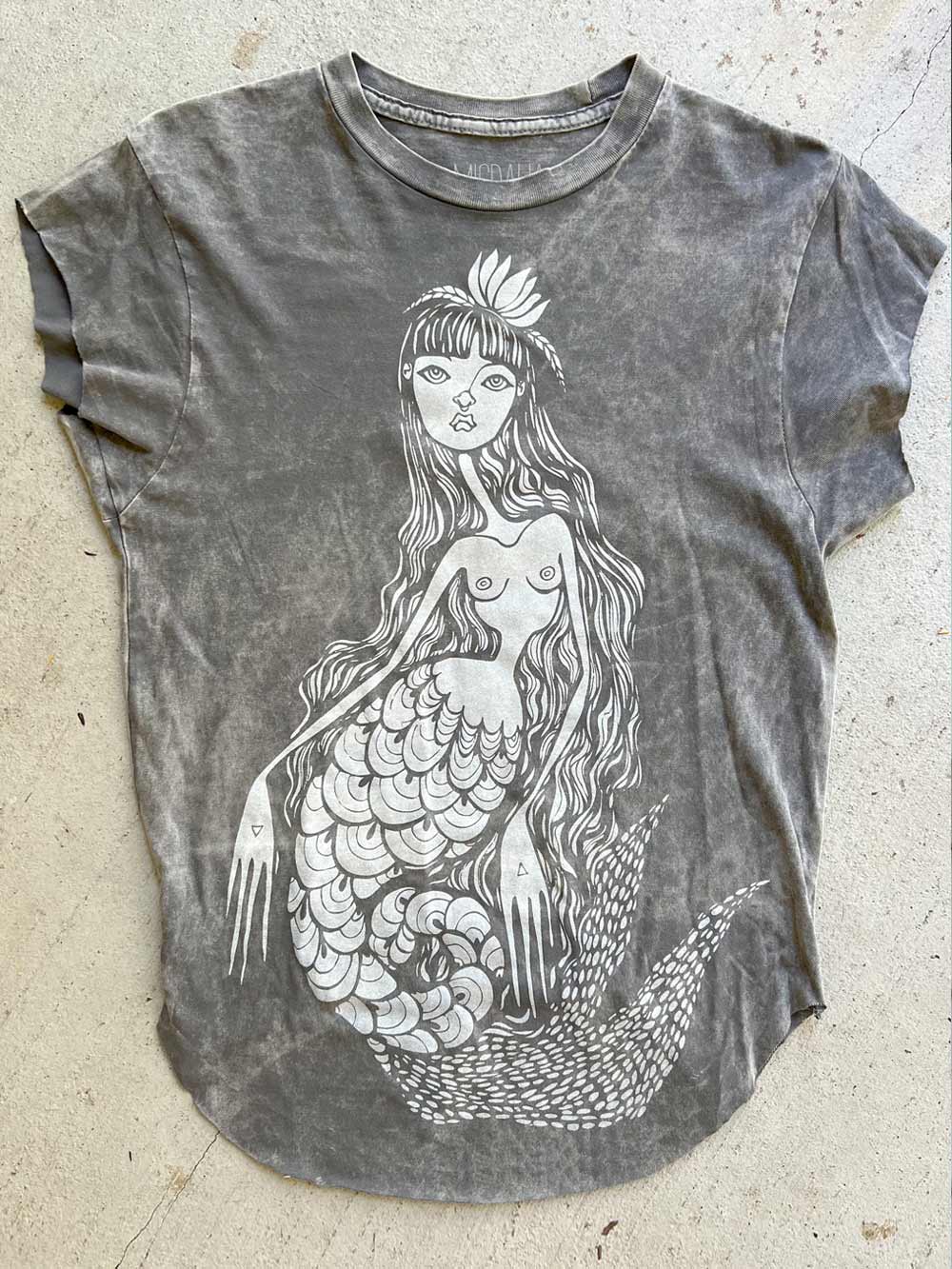 Gray t-shirt with a mermaid design on a concrete surface