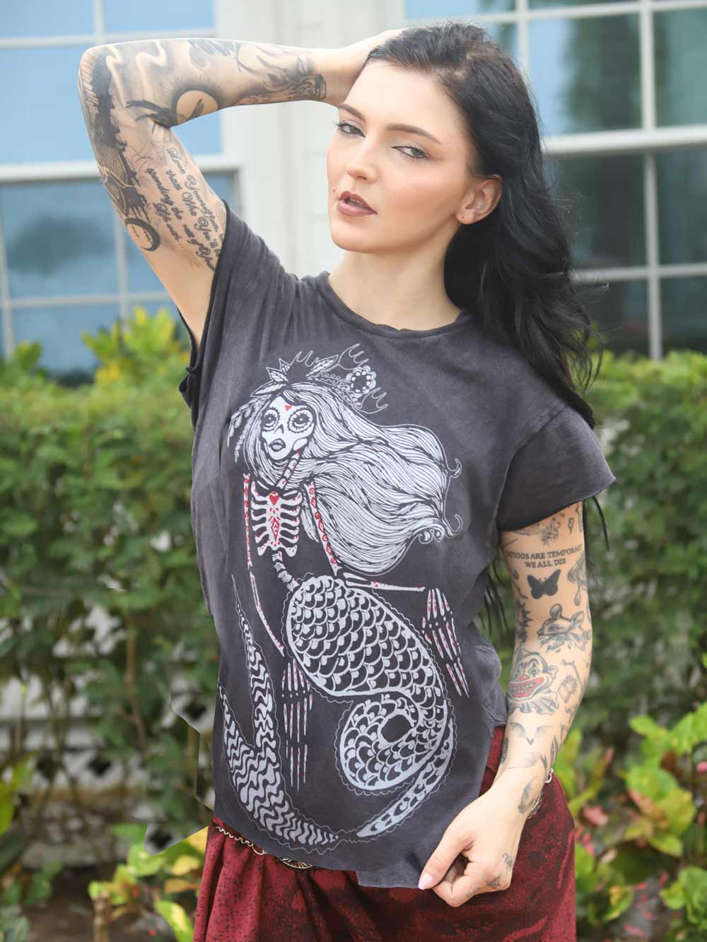 Woman wearing a black t-shirt with a white skeleton mermaid design outdoors.