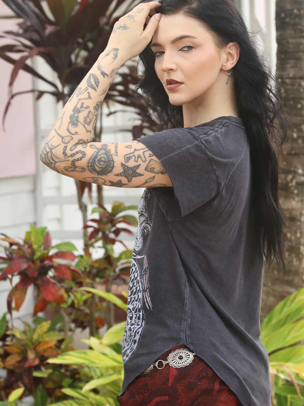 Model with tattoos wearing a dark gray t-shirt and red skirt outdoors.