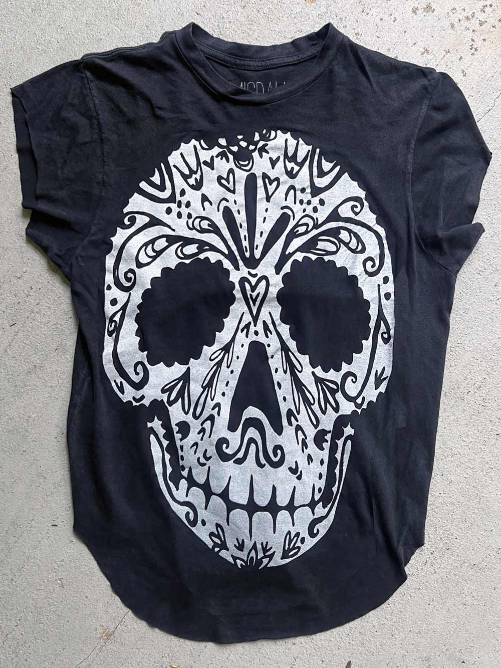 Black t-shirt with a white skull design on a concrete surface