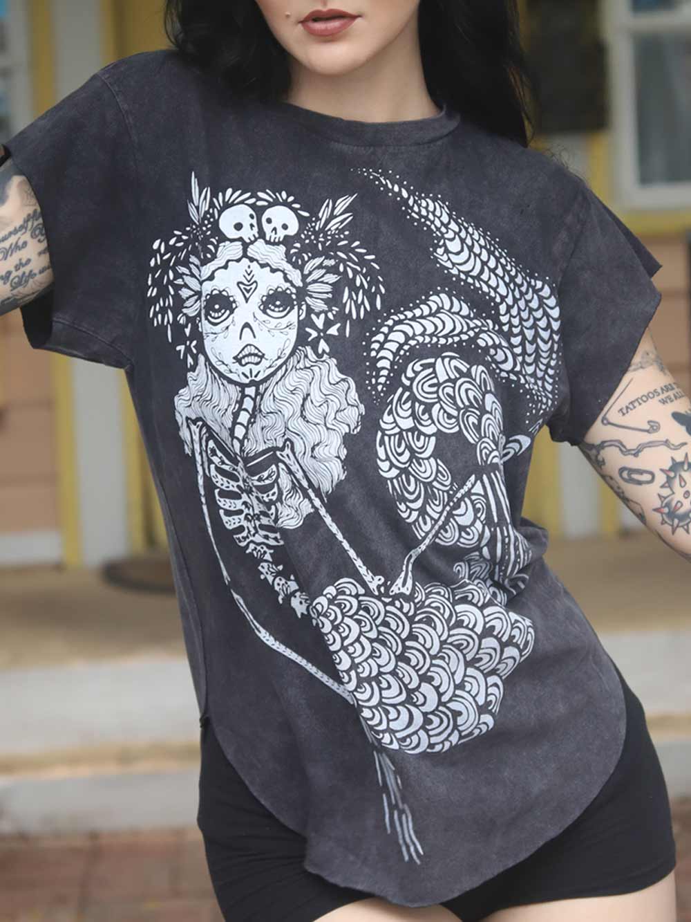 Model wearing a dark t-shirt with a white graphic design of a sugar skull mermaid.