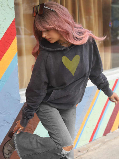 Lady wearing a dark hoodie with a gold heart design against a colorful background
