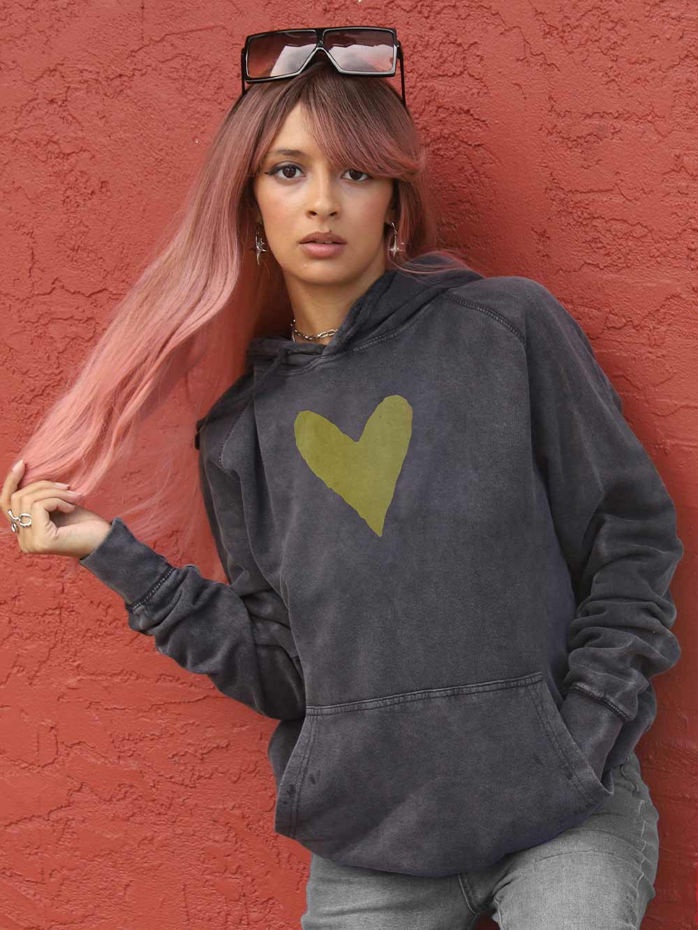 Woman wearing a faded black hoodie with a gold heart design against a red wall