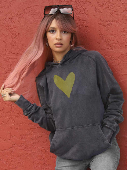 Woman wearing a faded black hoodie with a gold heart design against a red wall