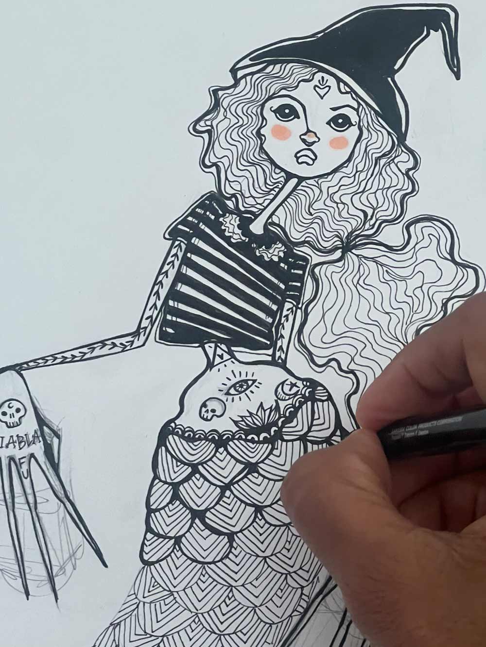 Hand-drawn illustration of a mermaid-like character with a witch's hat and tattooed arm, being completed by a hand holding a pen.