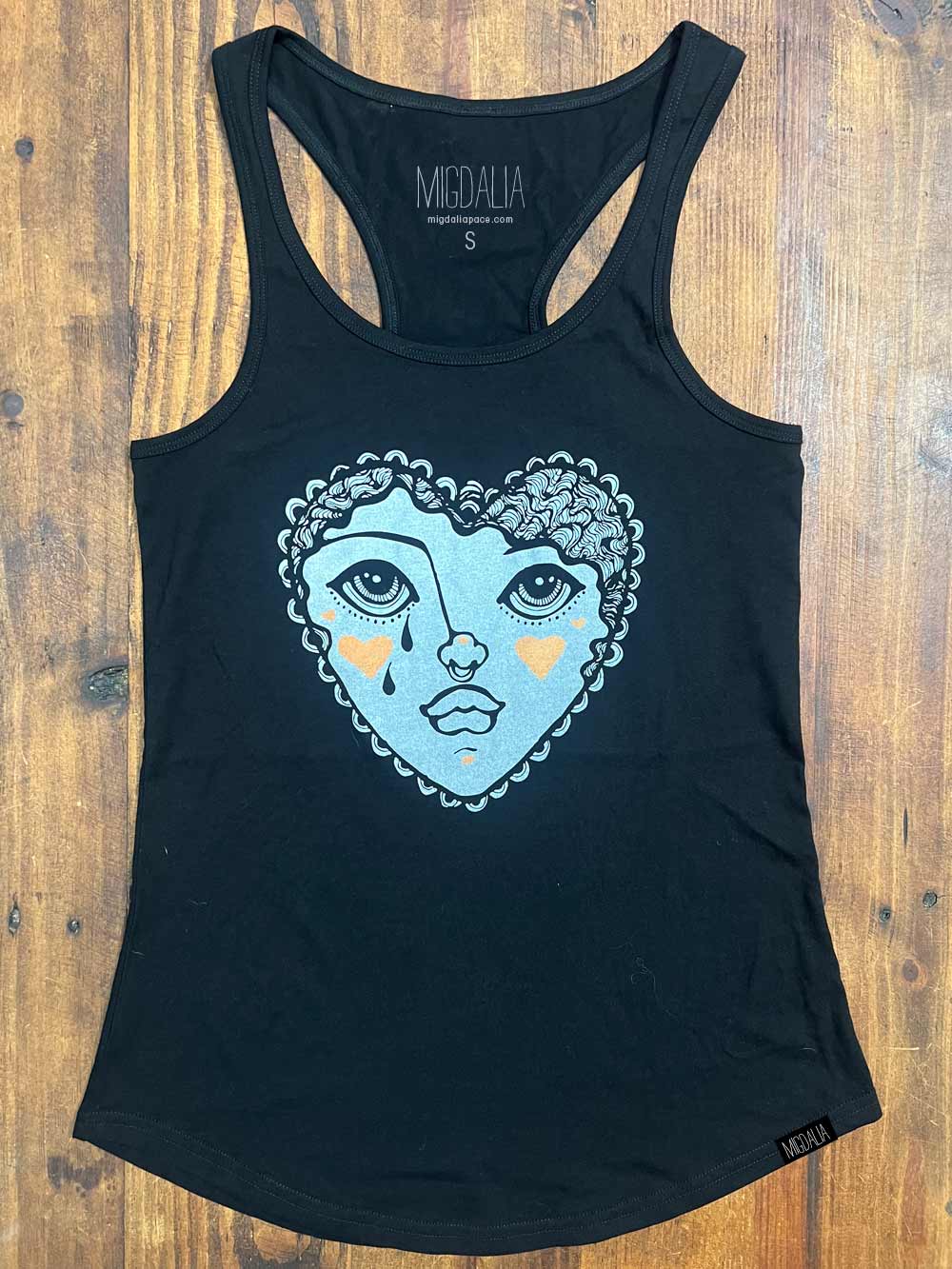 Black tank top with a blue heart-shaped face design on a wooden surface