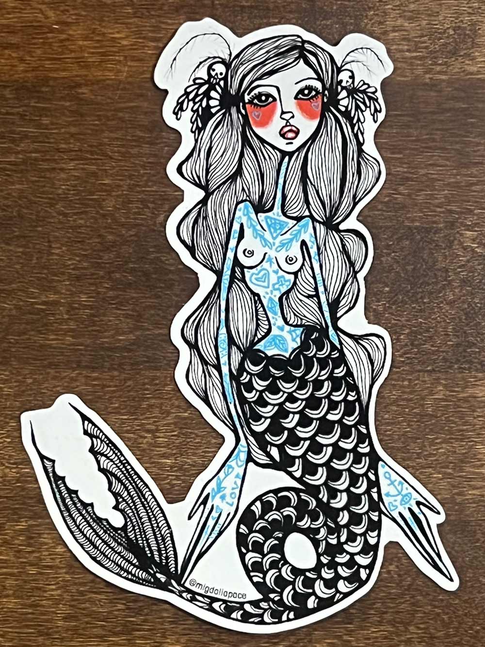 Sticker of a mermaid with a blue tattoos on a wooden surface