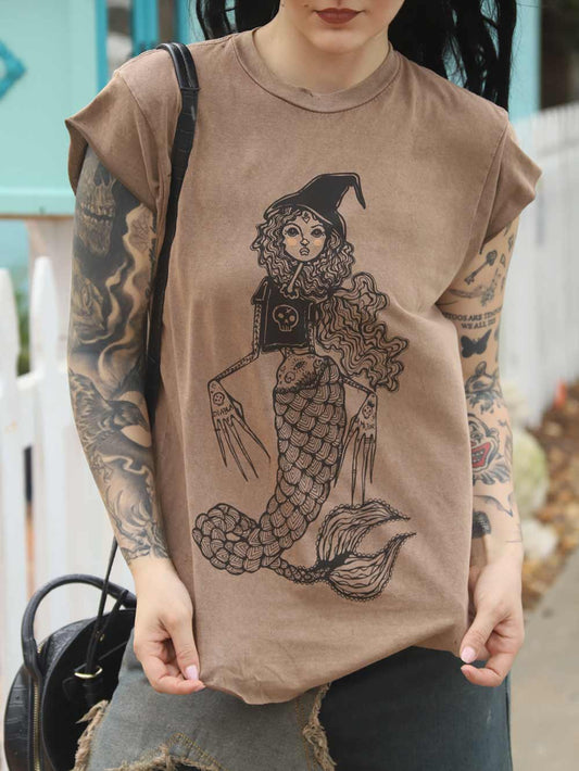Woman wearing a brown t-shirt with a mermaid and witch design.