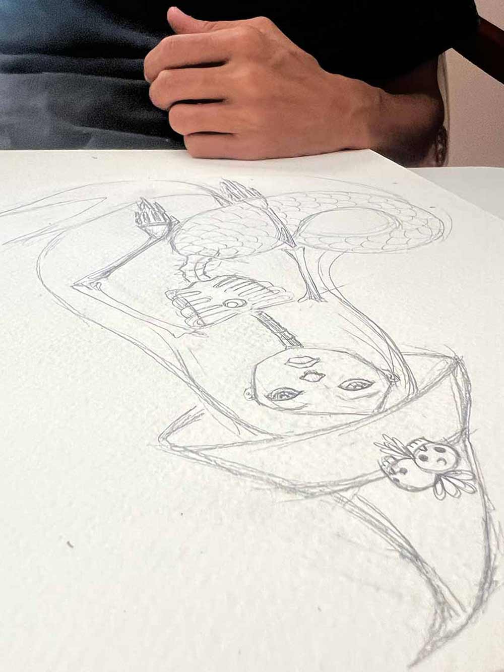 Pencil drawing of a witch mermaid character on a white sheet of paper with a hand resting above.