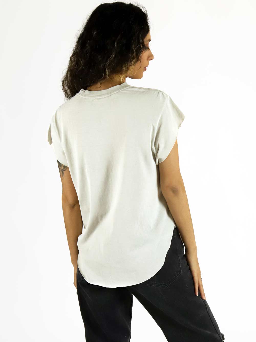 Person wearing a plain white t-shirt and dark pants on a white background. She is facing away and can see back of shirt.