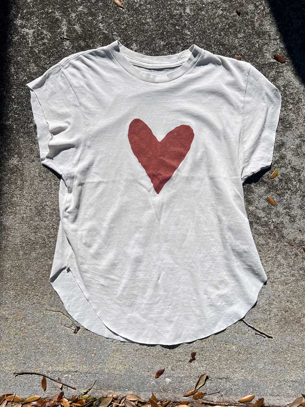 White t-shirt with a red heart design on a concrete surface