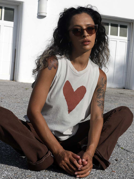 Model wearing a sleeveless shirt with a red heart design, sitting on the ground.