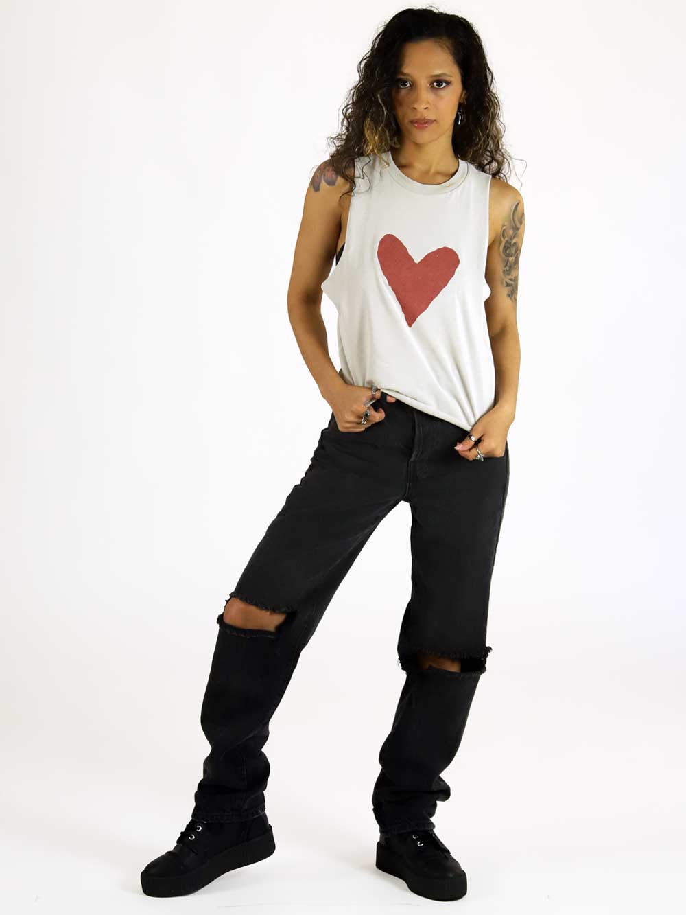 Woman wearing a sleeveless top with a red heart design and black pants on a white background