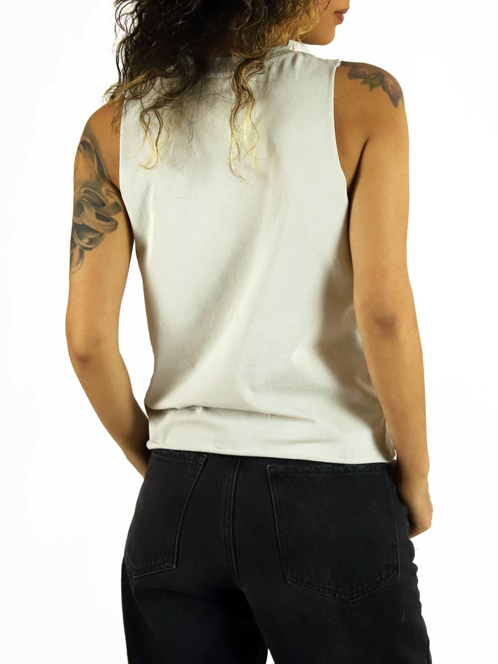 Woman wearing a white sleeveless top facing backwards and black pants on a white background