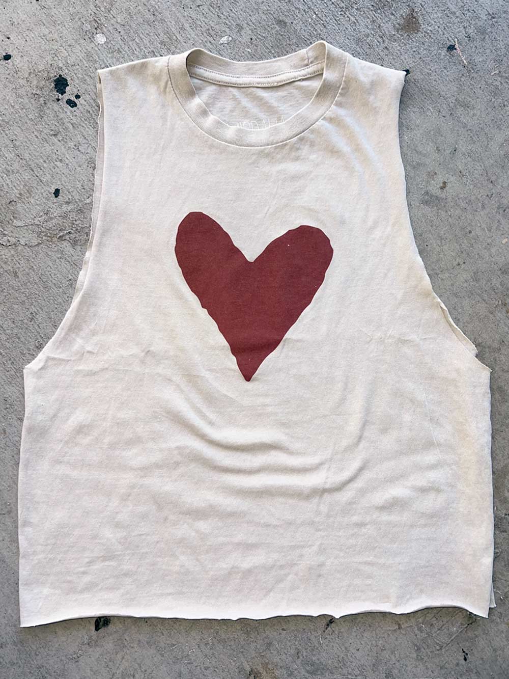 White sleeveless shirt with a red heart design on a concrete surface