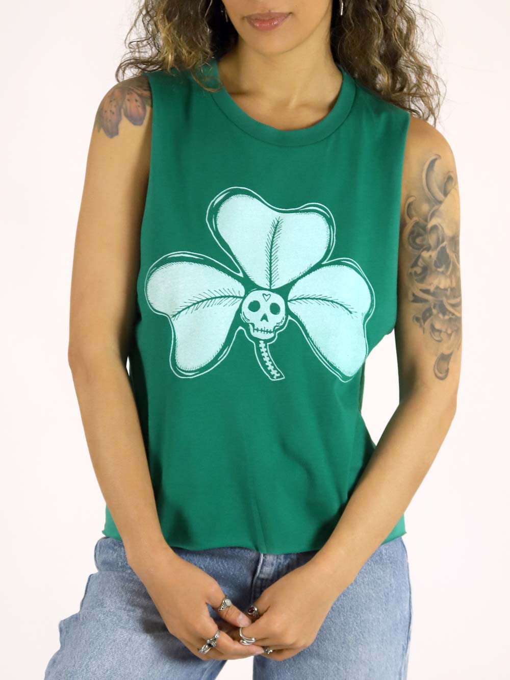 Woman wearing a green sleeveless shirt with a light skull and four-leaf clover design on a beige background