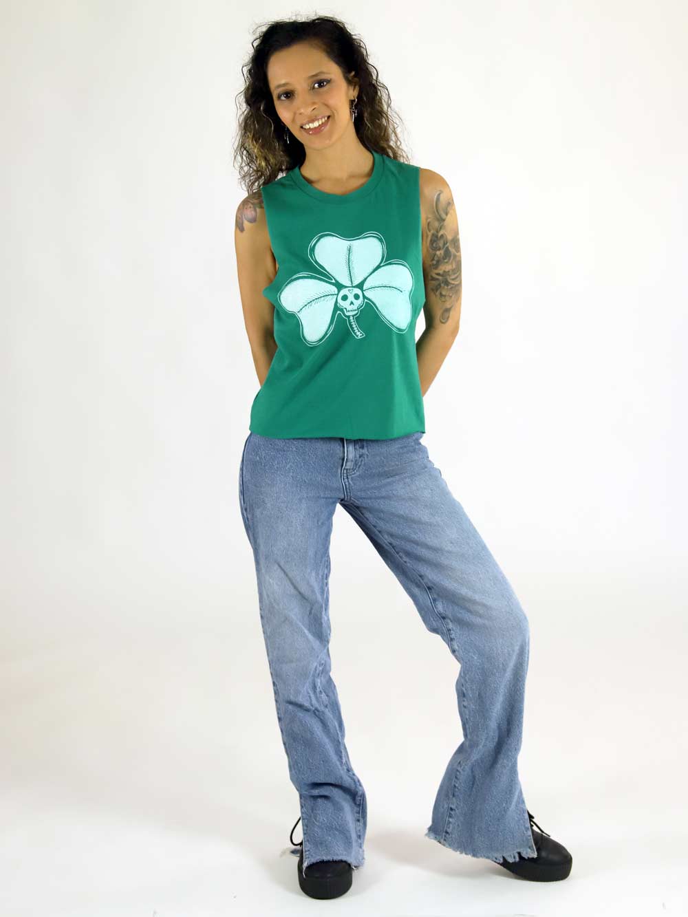 Woman wearing a green tank top with a white clover design and blue jeans on a white background