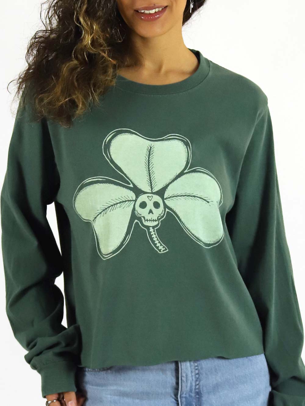 Green longsleeve crop with a skull and clover design worn by a woman on a white background