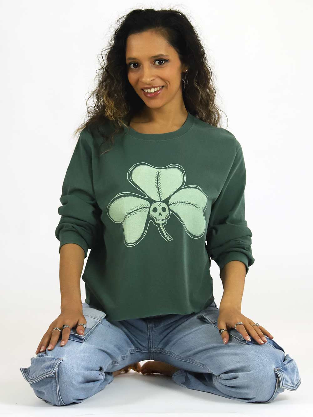 Woman wearing a green long sleeve crop with a clover design sitting on the floor.