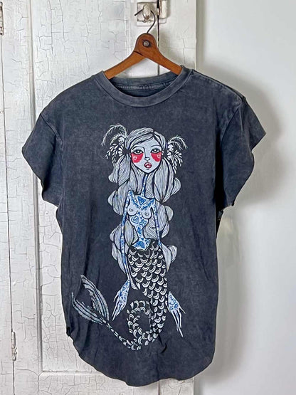 Dark gray t-shirt with a mermaid graphic on a wooden hanger against a white wall.