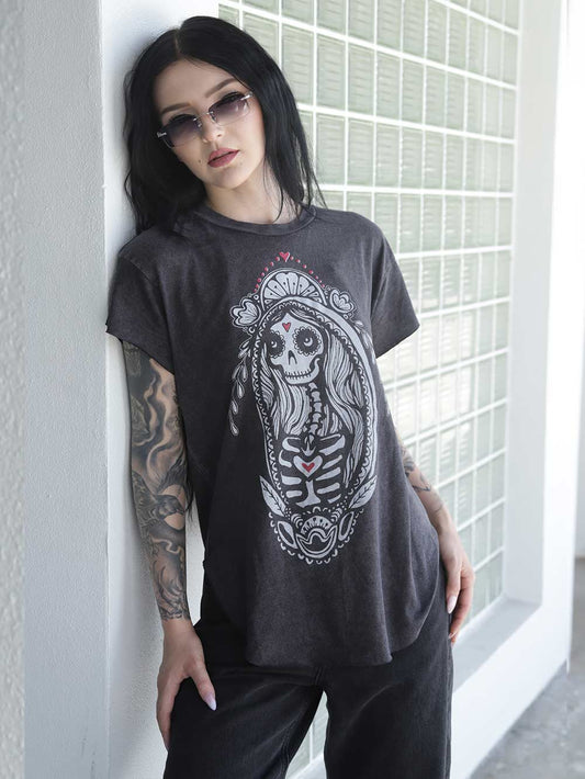 Woman wearing a black t-shirt with a sugar skull Madonna Graphic, standing against a glass wall.