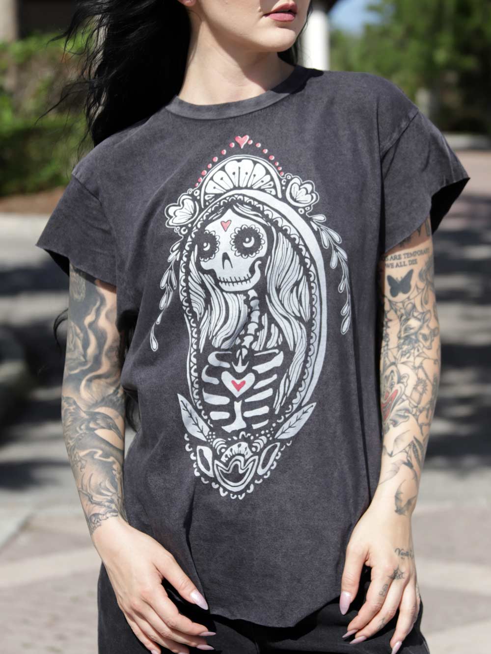 Woman wearing a dark gray t-shirt with a skeleton design outdoors.