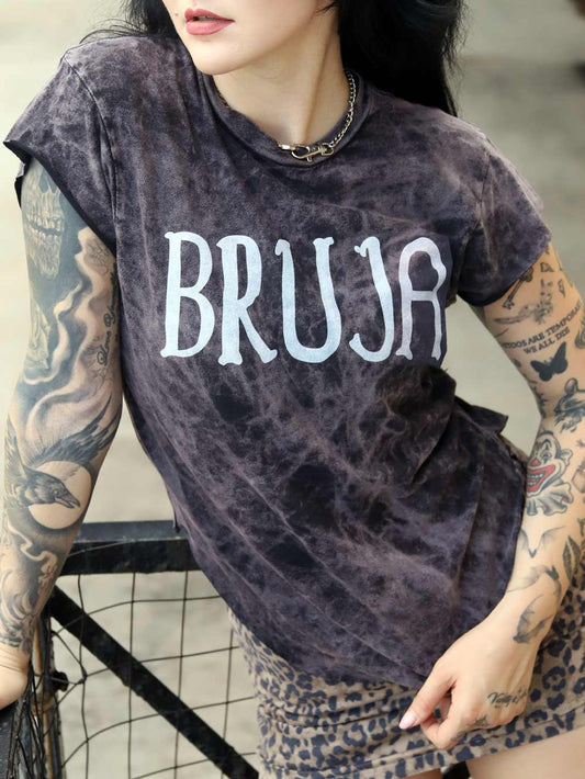 Woman wearing a t-shirt with 'BRUJA' text and tattoos on arms.