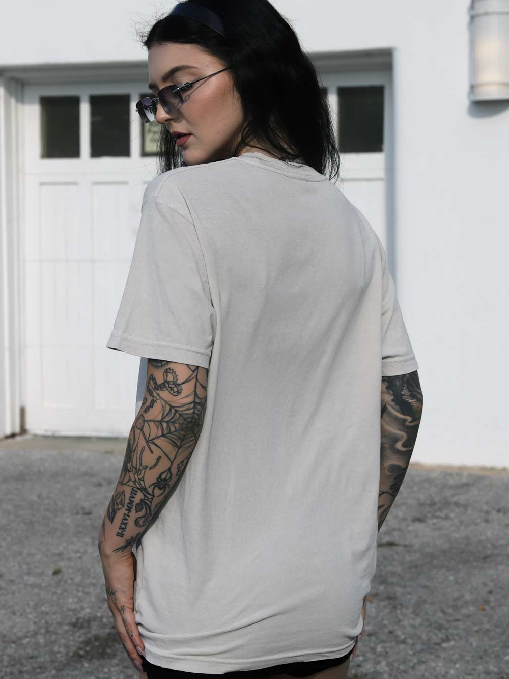 Person wearing a white t-shirt with tattoos on arms, standing outdoors.