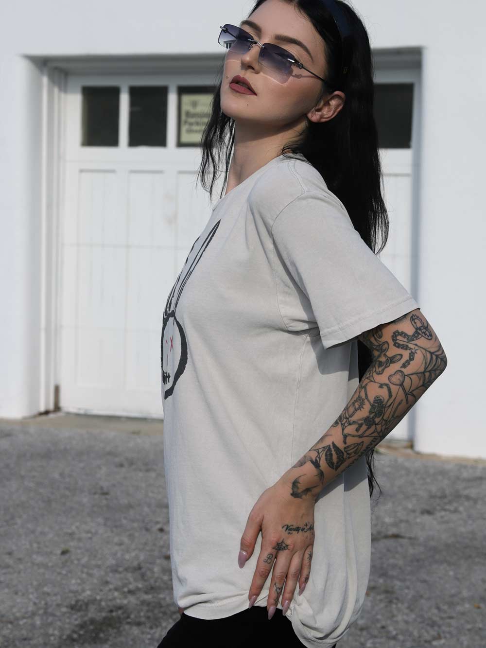 Person wearing a arctic color t-shirt with a graphic design, standing in front of a white building.