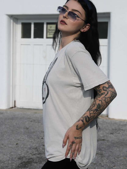Person wearing a arctic color t-shirt with a graphic design, standing in front of a white building.