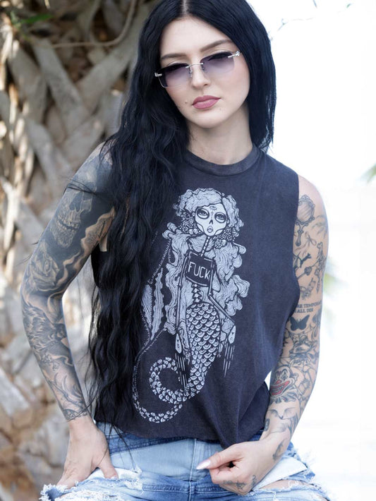 Woman wearing a sleeveless black top with a graphic design of a skeleton Mermaid wearing a shirt with the word fuck on it, sitting outdoors.